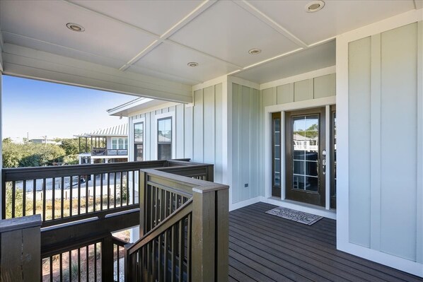 A covered outdoor deck with a wooden railing, a glass door entrance, and a view of the surrounding landscape.
