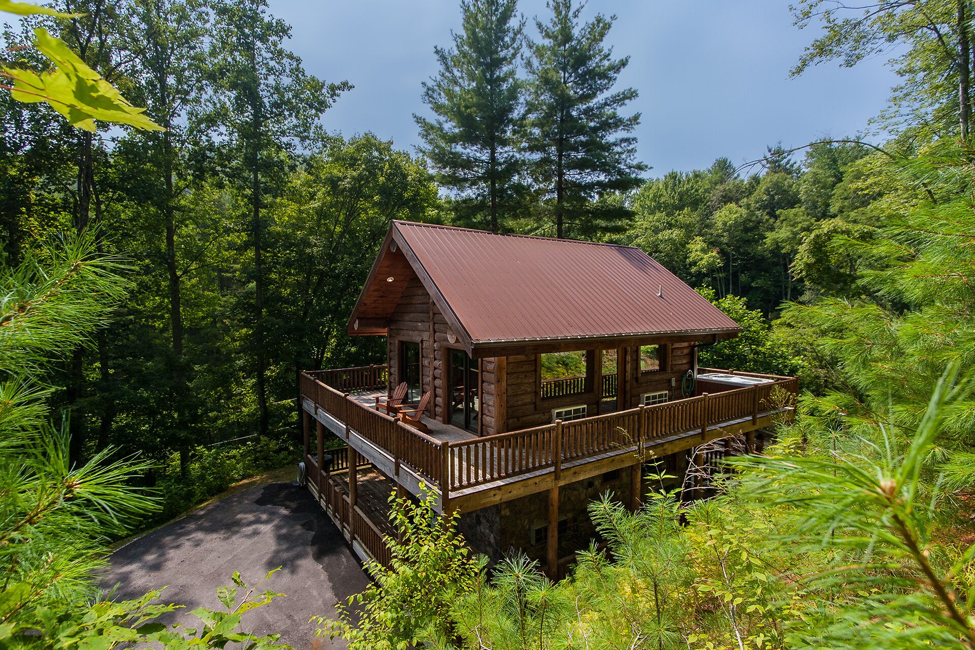 A cabin with a wooden deck and a covered porch, surrounded by dense forest.