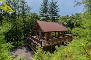 Une cabane dotée d’une terrasse en bois et d’un porche abrité, entourée d’une forêt dense.