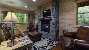 A cozy cabin interior with a stone fireplace, leather furniture, and a television mounted above it. - Black Bear Pond log cabin (Almond)