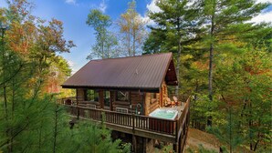 A log cabin with a hot tub on a deck surrounded by trees. - Black Bear Pond log cabin (Almond)