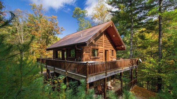 A wooden cabin with a deck, surrounded by dense forest. - Black Bear Pond log cabin (Almond)
