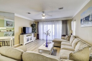 Relax in this inviting living room with a comfortable sofa, coffee table, and TV, surrounded by natural light and lush greenery.