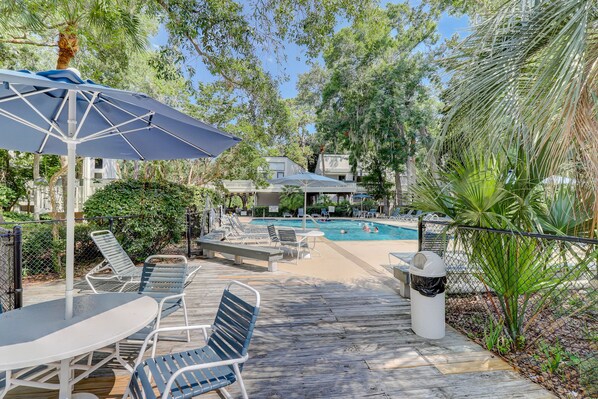 Relax by the pool surrounded by lush greenery and shaded by a large umbrella.