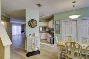 A spacious living area with a dining table and chairs, a kitchen with white cabinets, and a large wall clock. - Sunset Rentals | Ocean Breeze 18 | Dog Friendly (Hilton Head Island)