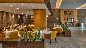 Un amplio espacio restaurante con sillas y mesas amarillas, un muro de piedra y un letrero que dice "PLAZA RESTAURANTE".