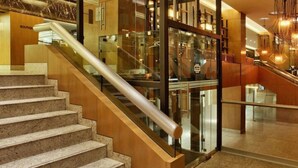Een moderne hotellobby met een marmeren trap, glazen balustrades en eigentijdse verlichtingsarmaturen.