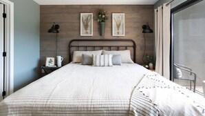 Un dormitorio con una cama grande, pared de madera, obras de arte enmarcadas y una ventana con cortinas.