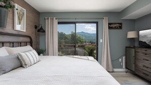 Un dormitorio con una cama grande, un aparador, un televisor y vistas a las montañas a través de un ventanal corredera.