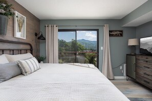 A bedroom with a large bed, a dresser, a lamp, and a view of mountains through a sliding door. - Walk 2 Downtown Gatlinburg/Gorgeous Mountain Views (Gatlinburg)