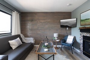 A modern living room with a dark leather sofa, a coffee table with a candle, a blue armchair, a fireplace, and a TV mounted on the wall. - Walk 2 Downtown Gatlinburg/Gorgeous Mountain Views (Gatlinburg)