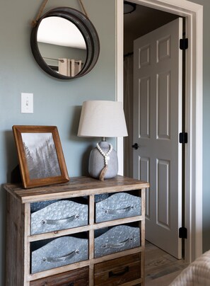 A room with a wooden cabinet with drawers, a mirror, a framed picture, and a lamp.