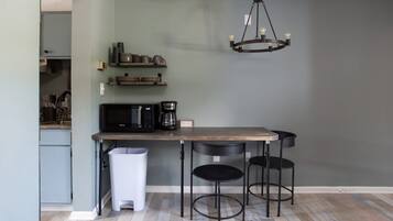 Une cuisine avec une table en bois, deux chaises noires, un luminaire suspendu et une poubelle.