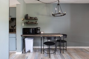 Una cocina con una mesa de madera, dos sillas negras, una lámpara colgante y un cubo de basura.