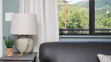 Una habitación con un sofá de cuero negro, una lámpara, un plano de evacuación enmarcado y vistas a un paisaje verde a través de una ventana.
