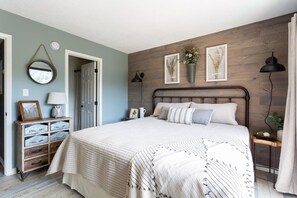 Un dormitorio con cama, mesitas de noche, cómoda, espejo y decoración mural.