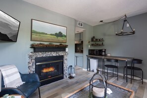 A living room with a fireplace, a dining area with bar stools, and a kitchen in the background. - Walk 2 Downtown Gatlinburg/Gorgeous Mountain Views (Gatlinburg)