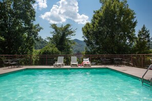 Piscina con sillas de descanso y vista a una montaña.