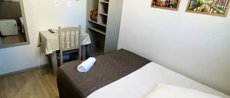 A hotel room with a bed, a desk, a chair, a television, and a wardrobe.