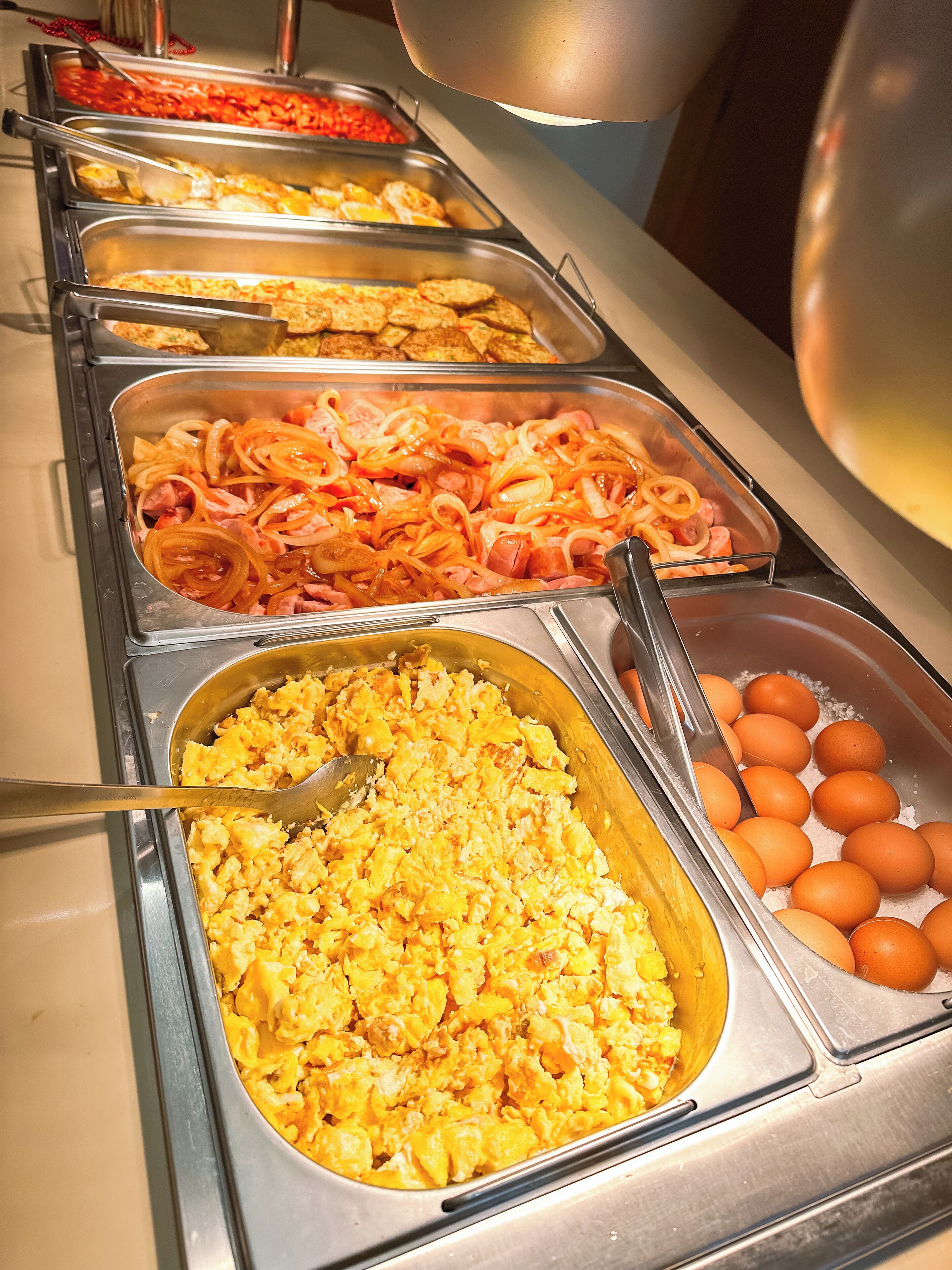 A buffet with various food options including scrambled eggs, sausages, and eggs.