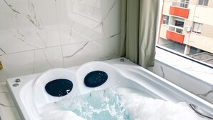 A hot tub with two jets, a marble-tiled floor, and a view of buildings outside. - Hotel Zata Econômico (Criciuma)