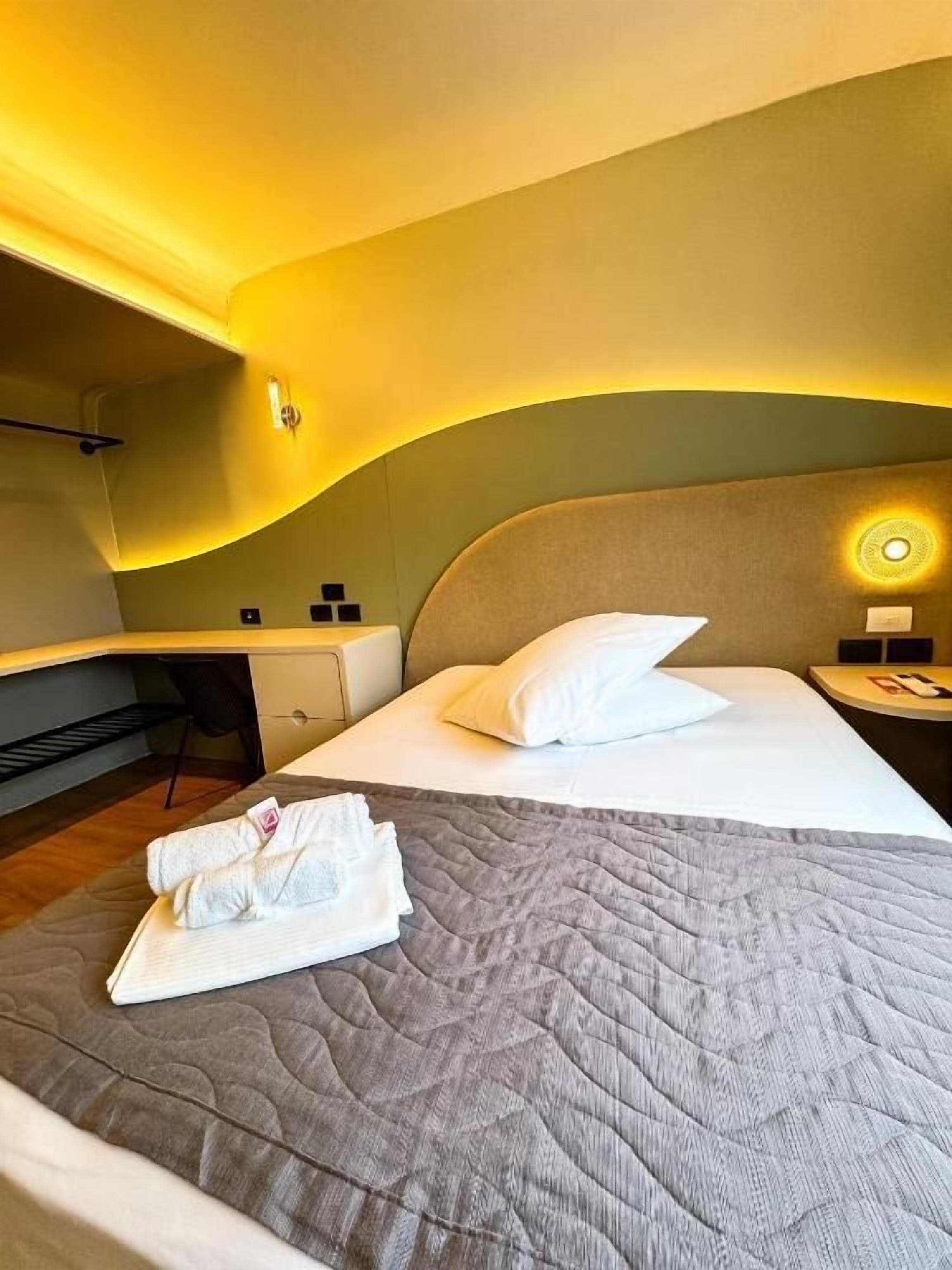 Una habitación de hotel con cama, escritorio y mesita de noche.