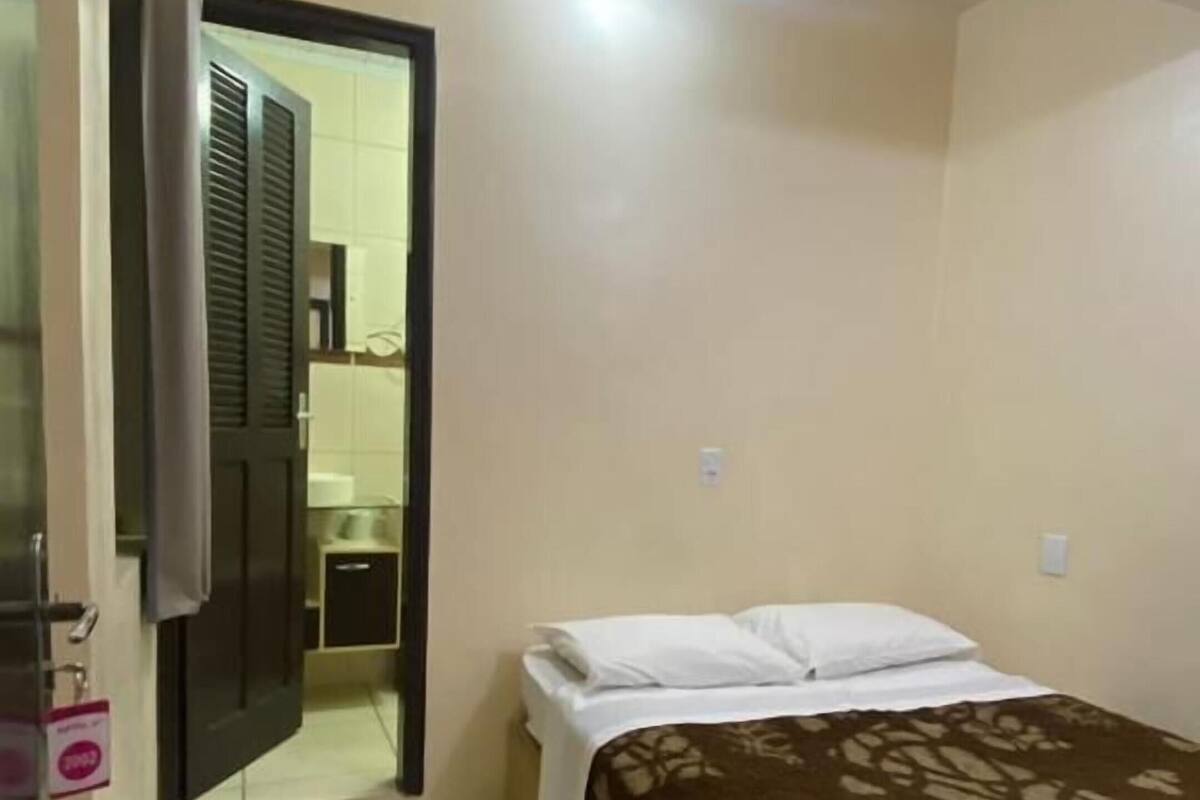 A bedroom with a bed, a bathroom visible through an open door, and a tiled floor.