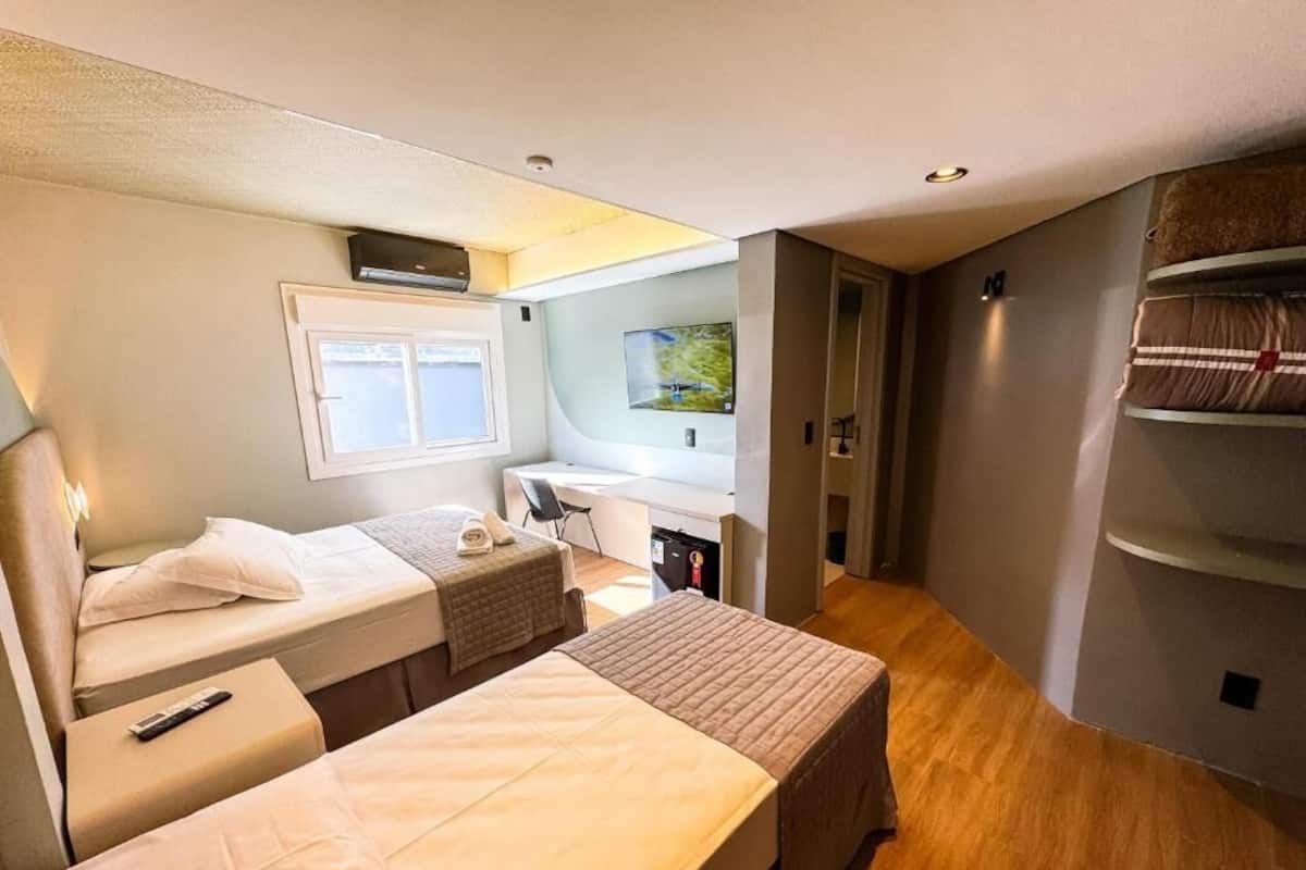 A compact bedroom with two beds, a desk, and a small kitchenette.