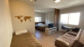 Una habitación de hotel compacta con una cama, un sofá, un televisor y una pequeña mesa de comedor.