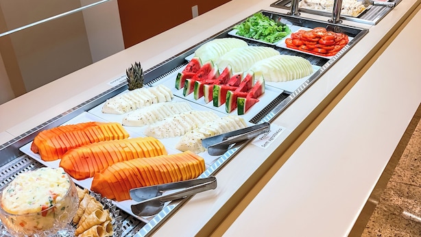 A buffet with various food items including sliced fruits, vegetables, and prepared dishes. - Hotel Zata Econômico (Criciuma)
