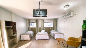 A modern hotel room with a central bed, two smaller beds, a yellow armchair, a TV, and a ceiling fan. - Hotel Zata Econômico (Criciuma)