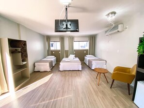 Una habitación de hotel moderna con una cama central, dos camas adicionales, un sillón amarillo, televisión y ventilador de techo.