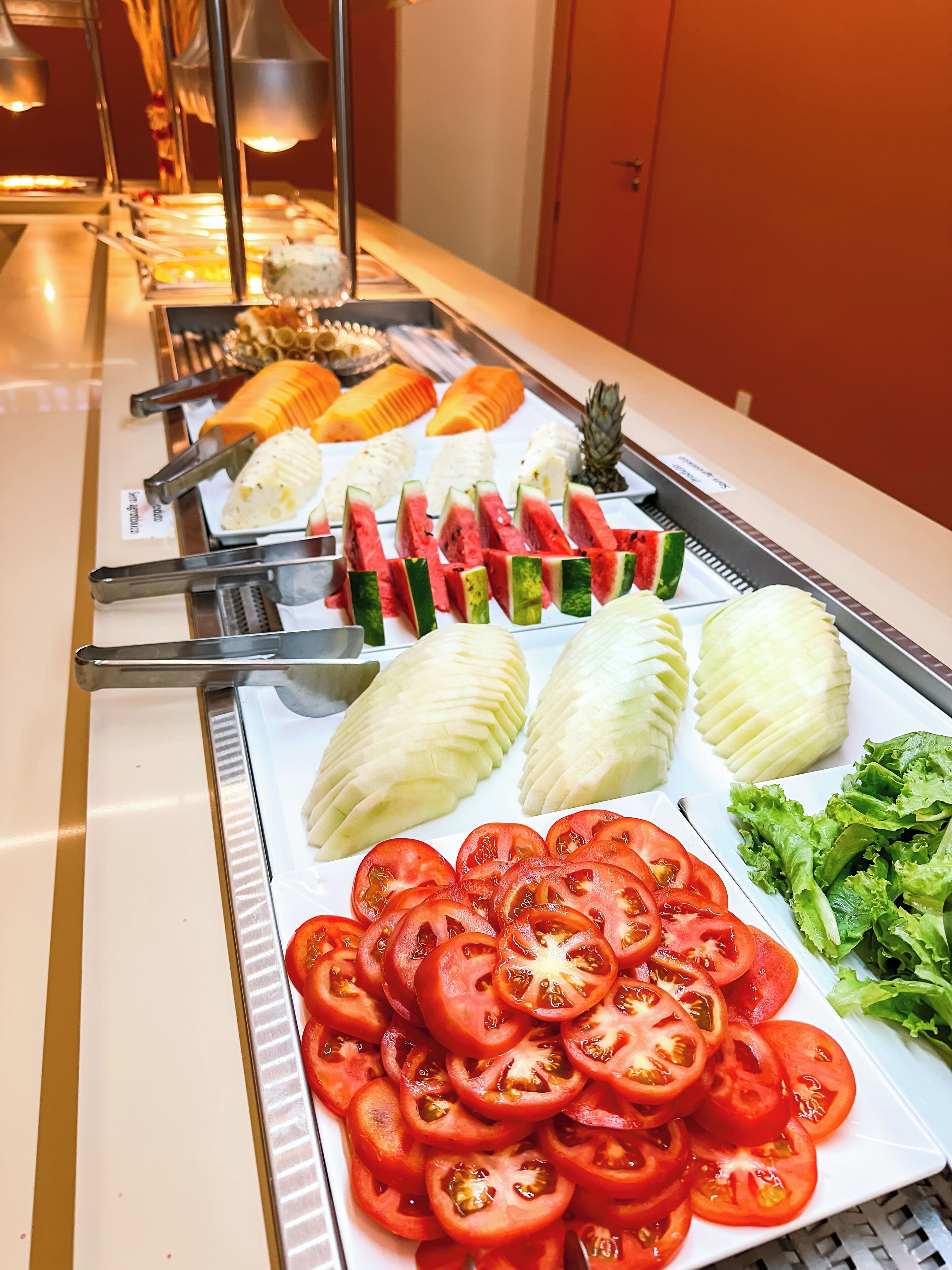 Un bufé con diversas opciones de comida, incluyendo sandía, melón y tomates en rodajas.