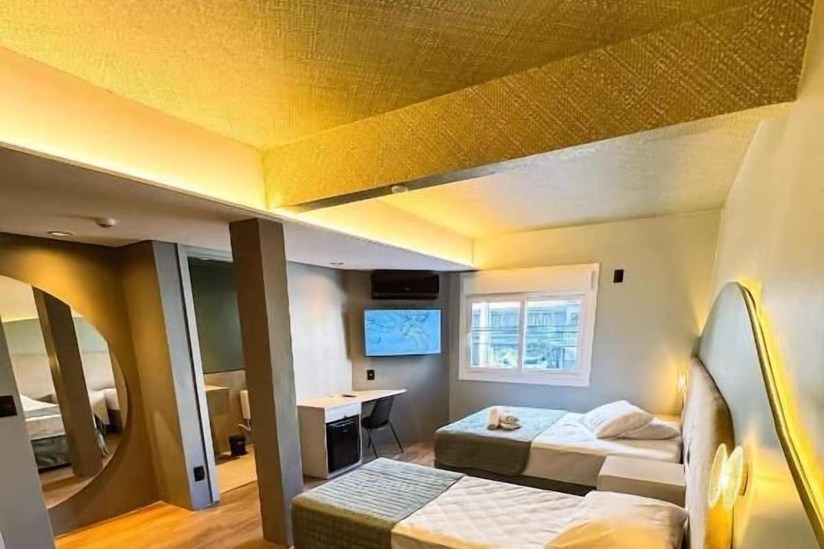 A compact hotel room with two beds, a desk, a chair, and a television.