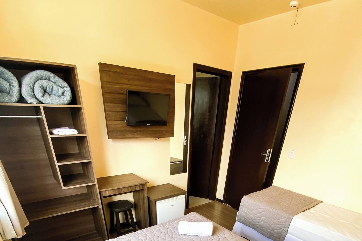 A hotel room with a bed, a desk, a chair, a TV, and a wardrobe.