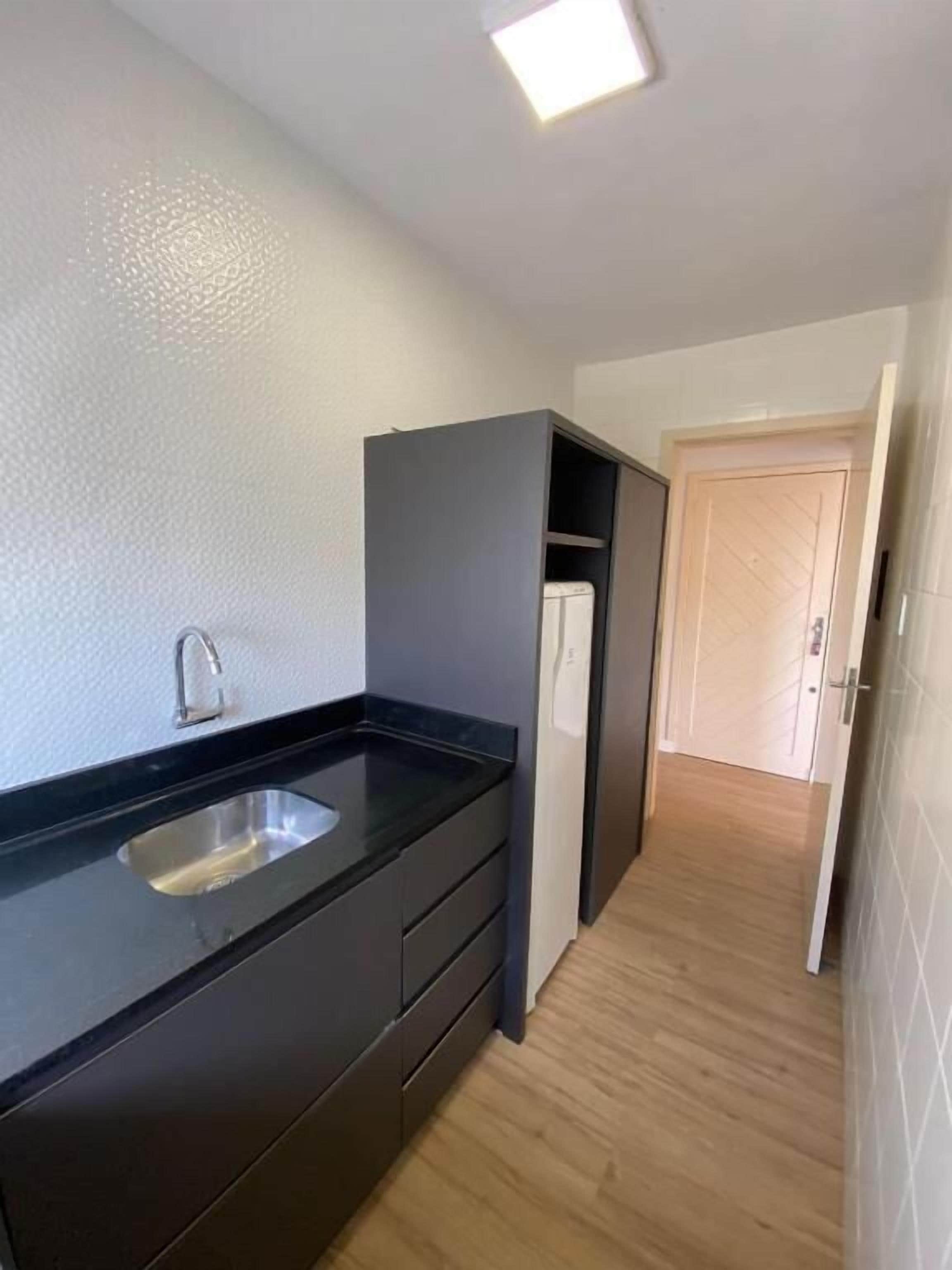 A compact kitchen with a black countertop, a stainless steel sink, and a built-in oven. A wooden door leads to another room.