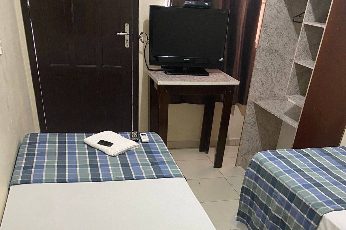 A room with two beds, a television on a stand, and a door.