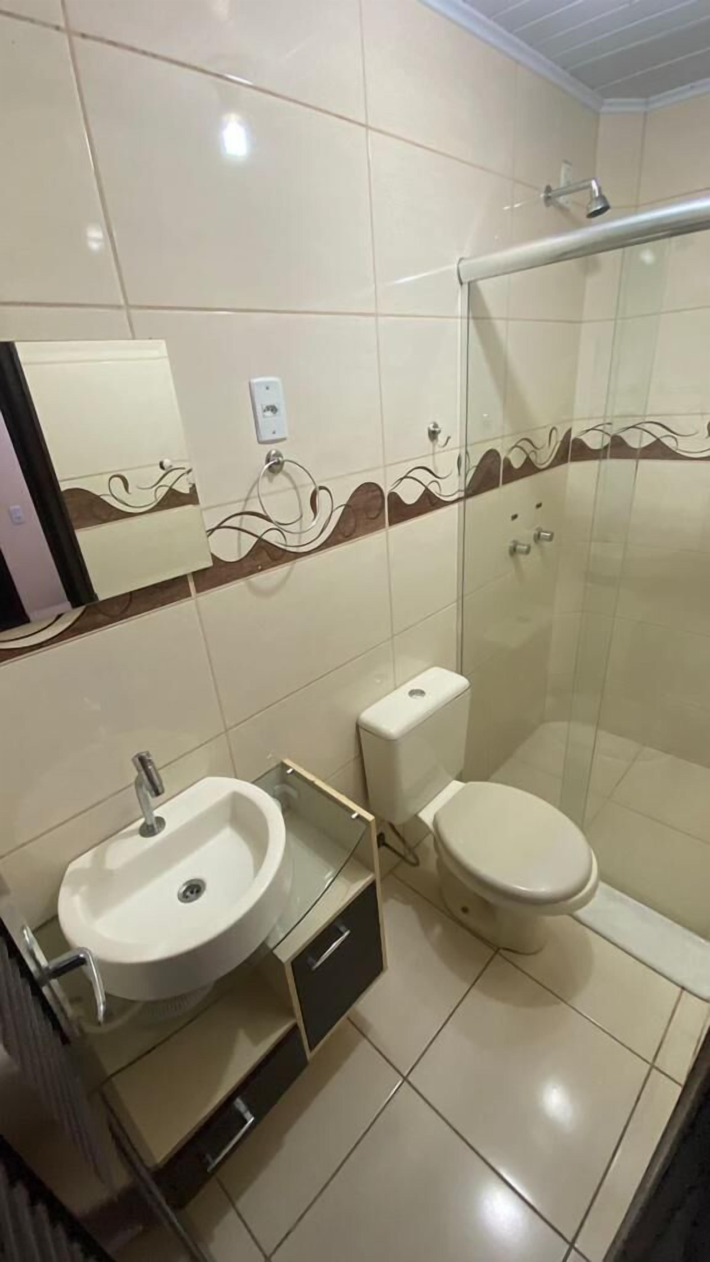 A bathroom with a glass shower enclosure, a toilet, and a sink with a mirror above it.
