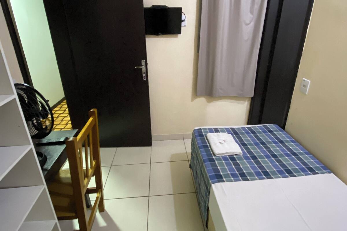 A small, compact room with a bed, a chair, a desk, and a television mounted on the wall.