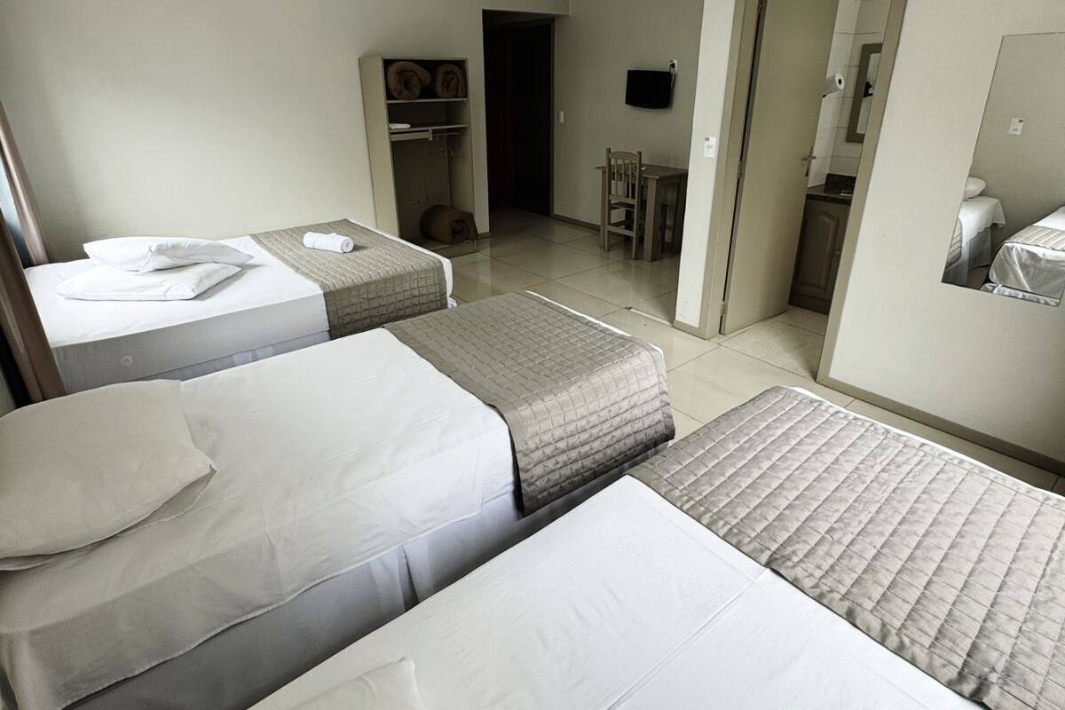 A hotel room with two beds, a desk, a chair, a wardrobe, and a bathroom visible through an open door.