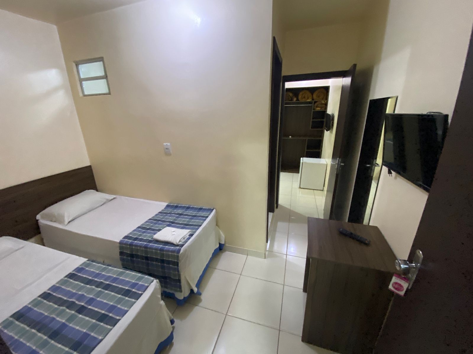A small hotel room with two single beds, a small table, a TV, and a mirror.