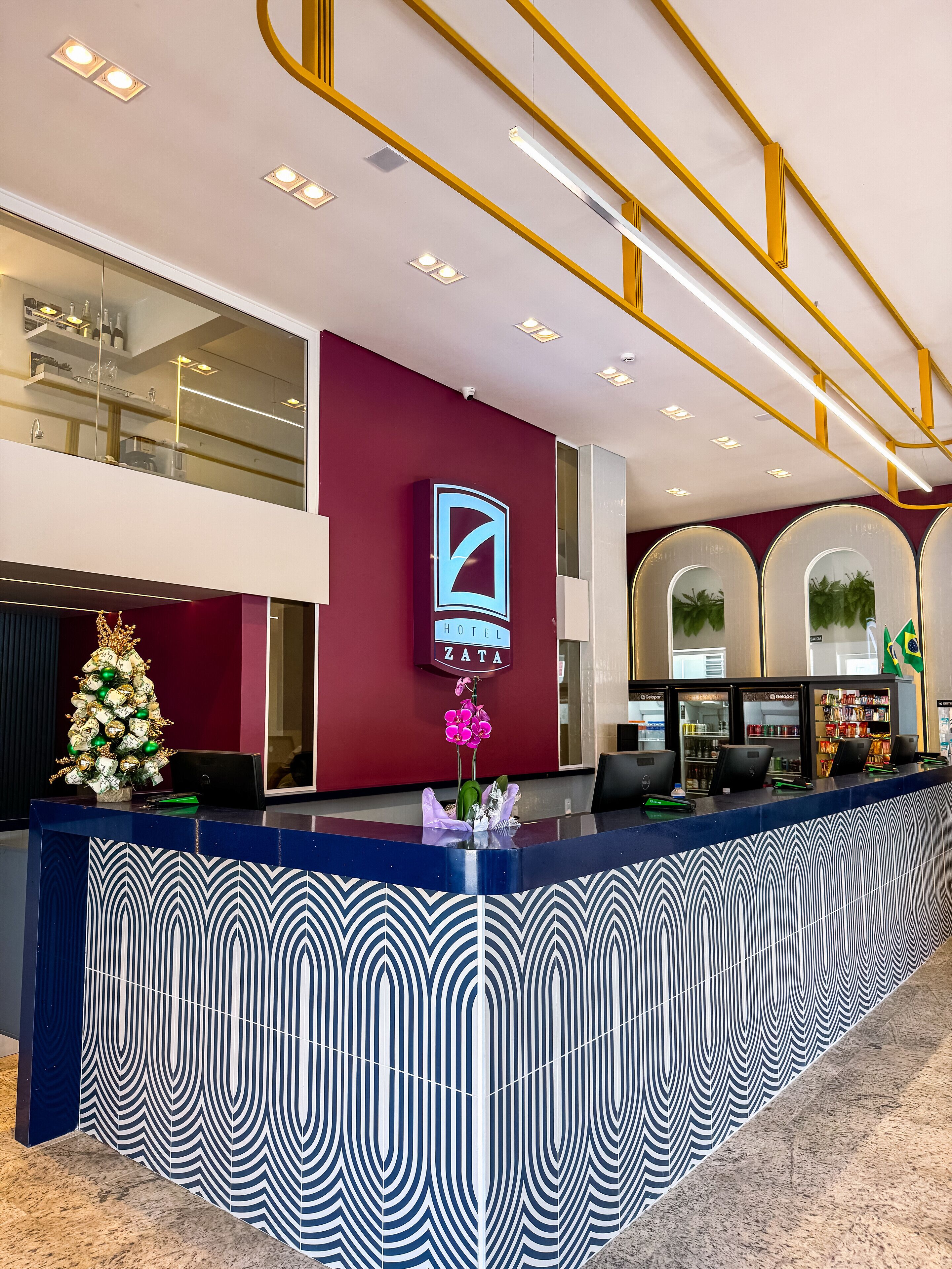 Zona de recepción de un hotel con diseño moderno, que incluye un mostrador de recepción, un árbol de Navidad y un logotipo en la pared.