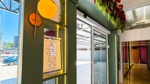 A hotel lobby with a reception desk, a glass door entrance, a yellow pendant light, and a decorative plant. - Hotel Zata Econômico (Criciuma)