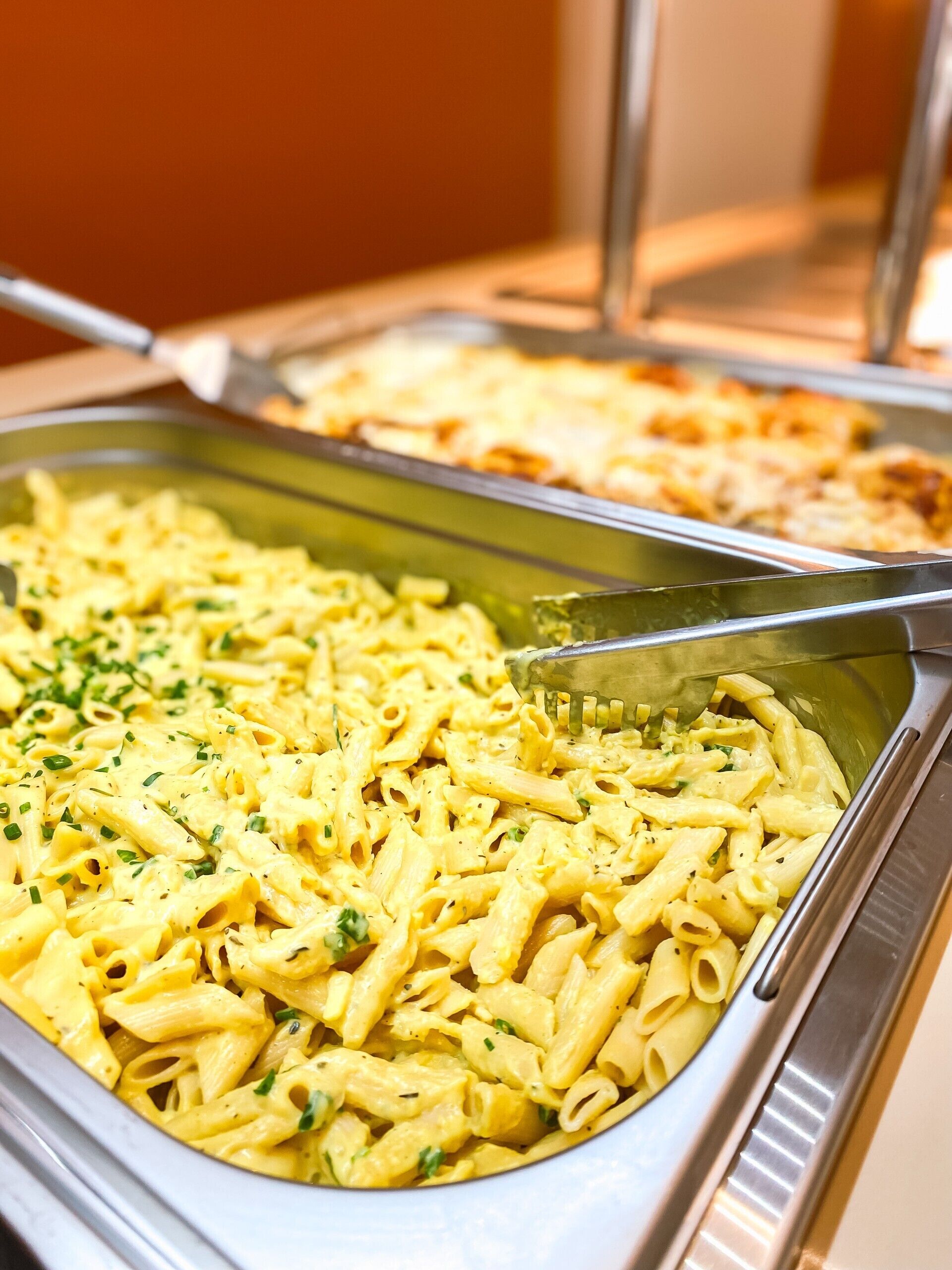 Un bufé con platos de pasta, incluyendo una pasta cremosa y un plato al horno.