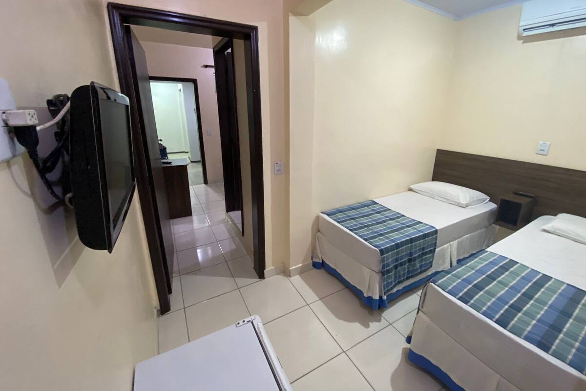 A hotel room with two beds, a TV mounted on the wall, and a refrigerator.
