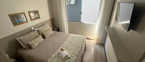 A hotel room with a bed, air conditioning unit, curtains, a television, and a window.