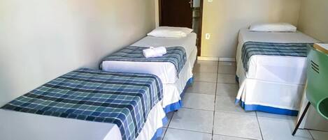A hotel room with two single beds, a small desk, and a television on the wall.