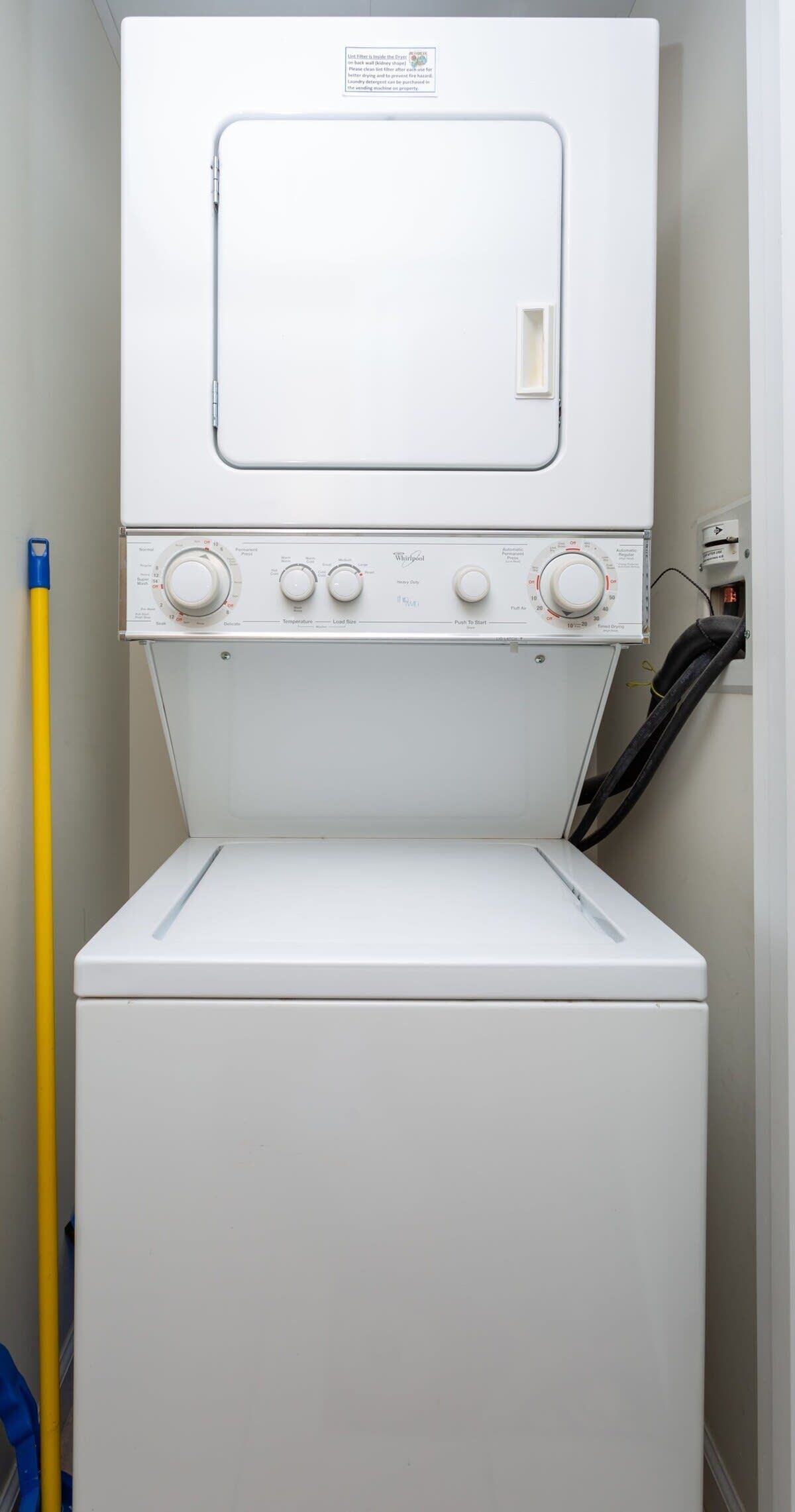 A front view of a Whirlpool washer with control knobs and a yellow mop handle beside it.