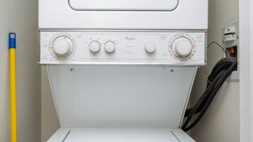 A front view of a Whirlpool washer with control knobs and a yellow mop handle beside it.