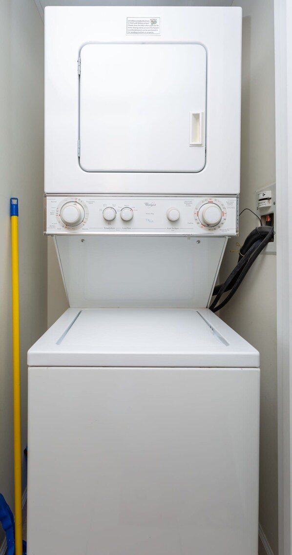 Vista frontal de una lavadora Whirlpool con perillas de control y un mango de mopa amarillo a un lado.